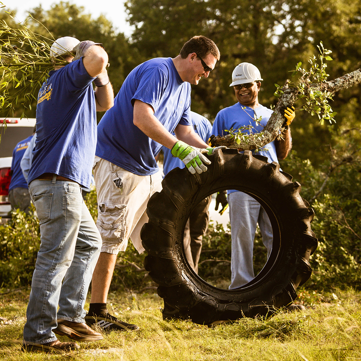 Image of three NuStar employees volunteering, picking up and transporting tree debris. 